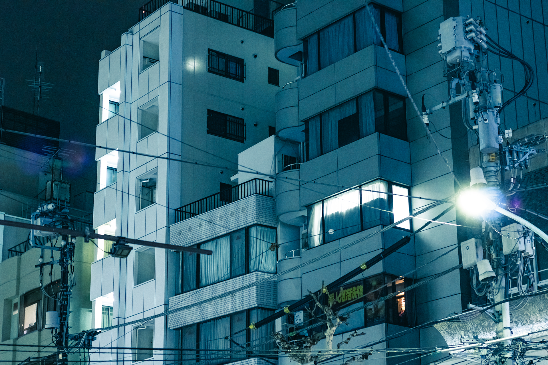 Pale blue modern building facade at night with wires crossing the foreground.